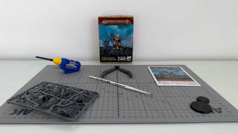 A Lord-Terminos sprue on a cutting mat, with a tube of plastic glue, clippers, a hobby tool, the instruction sheet, two bases and the box behind.